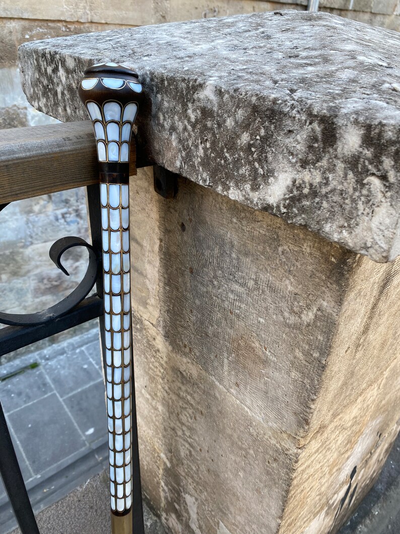 Puede incluir: Un bast&oacute;n blanco y marr&oacute;n con una parte superior decorativa hecha de azulejos de n&aacute;car blanco.