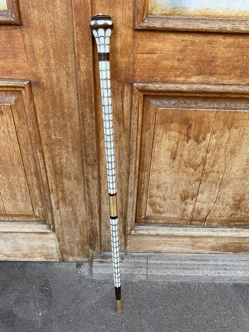 Puede incluir: Un bast&oacute;n blanco y dorado con una parte superior decorativa. El bast&oacute;n est&aacute; hecho de madera y tiene un patr&oacute;n blanco y dorado.