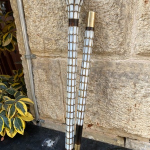 Puede incluir: Dos bastones de paseo con incrustaciones decorativas de n&aacute;car. La parte superior de los bastones es de madera oscura y tiene una punta de metal dorado. Los bastones est&aacute;n de pie contra una pared de piedra.