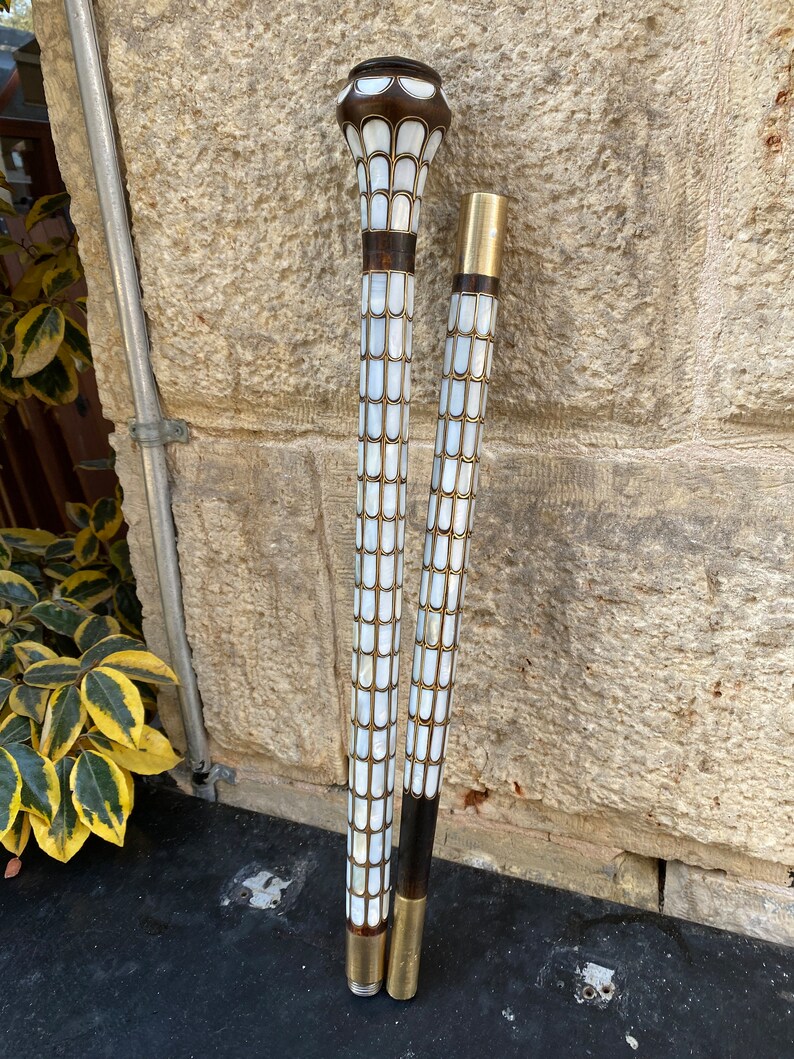 Puede incluir: Dos bastones de paseo con incrustaciones decorativas de n&aacute;car. La parte superior de los bastones es de madera oscura y tiene una punta de metal dorado. Los bastones est&aacute;n de pie contra una pared de piedra.