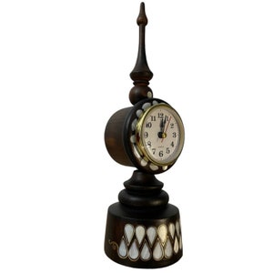 Può includere: Un orologio da tavolo in legno scuro con un quadrante bianco e dettagli dorati. L'orologio è decorato con intarsi di madreperla e ha un'alta guglia appuntita.