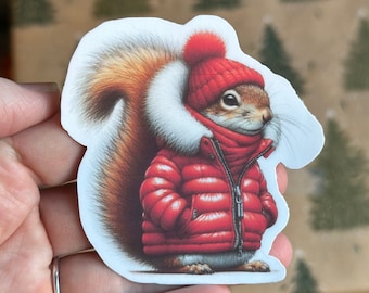 May include: A red squirrel wearing a red puffer jacket with a white fur trim and a red knitted hat with a white pom pom.