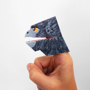 May include: A gray paper finger puppet of a gorilla with a white mouth and red teeth. The gorilla has a black eye and a brown eyebrow.