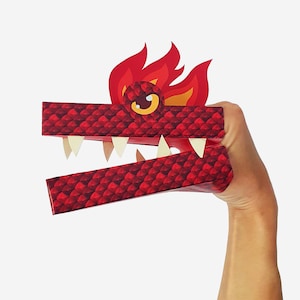 May include: Red paper dragon puppet with a fire mane and a toothy grin. The puppet is held by a hand, ready for play.