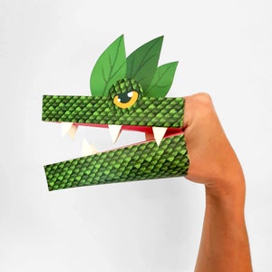 May include: Green and white paper puppet of a crocodile with a pink mouth and sharp teeth. The puppet is designed to be worn on a finger.