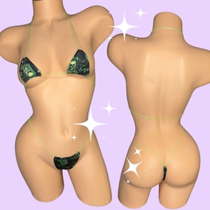 May include: A two-piece bikini set with a black and green skull print. The bikini top is a triangle style with thin, neon green straps. The matching bottom is a thong style, also with neon green straps. The set is displayed on a mannequin.