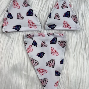 May include: Three pieces of lingerie with a white background and a repeating pattern of pink and blue diamonds. The lingerie pieces are triangle-shaped and appear to be a bra and a thong.