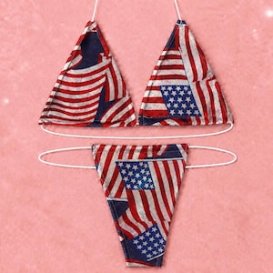 Puede incluir: Un conjunto de bikini de dos piezas con un estampado patriótico de la bandera estadounidense con rayas y estrellas rojas, blancas y azules. La parte superior consta de dos copas triangulares con finos lazos blancos.