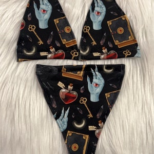 May include: Black lingerie set with a repeating pattern of a blue hand with a red eye, keys, potion bottles, and spell books. The set includes a triangle top and a matching bottom.