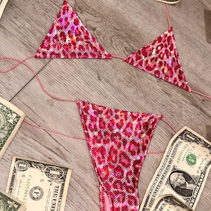 May include: Pink leopard print bikini with a triangle top and a high-cut bottom. The bikini is made of a shiny, iridescent fabric.
