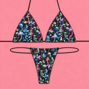 May include: A black bikini set featuring a vibrant, iridescent mushroom and star pattern. The top consists of two triangular cups with thin black string ties, and the bottom is a high-cut thong style with matching thin black side ties.