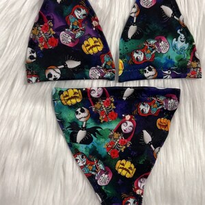 May include: A three-piece lingerie set featuring a colorful print with characters and imagery from The Nightmare Before Christmas. The set includes a triangle-style top and a low-rise bottom. The fabric has a dark background with Jack Skellington, Sally, and pumpkins.