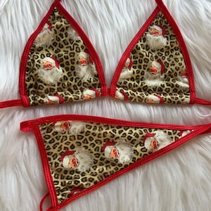 Peut inclure: Ensemble de bikini deux pièces avec un imprimé léopard et des visages de Père Noël. Les bords sont bordés de tissu rouge. Le haut est de style triangle et le bas est de style string.