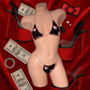 May include: A black bikini featuring a Hello Kitty design, alongside red platform heels and a matching bow. The image also includes US $100 bills and a silver chain bracelet, set against a red background.