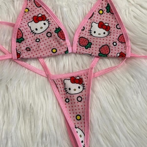 Puede incluir: Conjunto de bikini rosa con estampado de Hello Kitty y fresas. La parte superior es de estilo triangular con tirantes ajustables y la parte inferior es de estilo atrevido con un lazo.