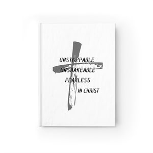 Puede incluir: Un cuaderno de tapa dura blanco con una cruz gris. La cruz está acompañada de las palabras "UNSTOPPABLE, UNSHAKEABLE, FEARLESS, IN CHRIST" en una fuente sans-serif en negrita. La portada del cuaderno es limpia y minimalista.