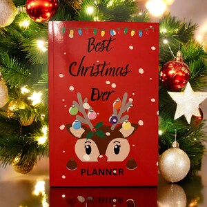 May include: Red planner with a reindeer illustration and the text "Best Christmas Ever" on the cover. The planner has a white background with snowflakes and a string of Christmas lights.