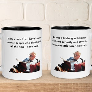 May include: Two white coffee mugs with black rims. The mug on the left features a quote about reading and the mug on the right features a quote about lifelong learning. Both mugs feature a black and white image of a man reading a book.