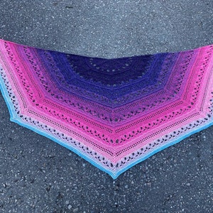 May include: A crocheted shawl with a gradient of pink, purple, and blue colors. The shawl is made with a delicate lace pattern and has a scalloped edge.