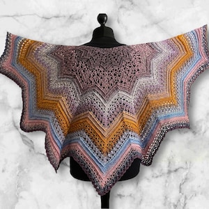 May include: A crocheted shawl with a multi-colored design featuring shades of pink, purple, blue, and yellow. The shawl is displayed on a mannequin.