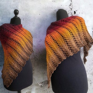 Può includere: Due scialli all'uncinetto in un gradiente di colori rosso, arancione e marrone. Gli scialli sono esposti su manichini.