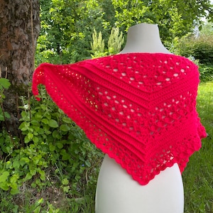 May include: A bright pink crocheted shawl with a lacy pattern. The shawl is draped over a white mannequin.