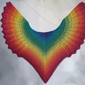 Peut inclure: Un châle tricoté triangulaire présentant un motif dégradé arc-en-ciel vibrant. Le textile affiche une texture de point chevron ou zigzag cohérente qui passe par des nuances de rouge, orange, jaune, vert, bleu et violet profond sur le tissu.