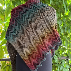 May include: A handmade crochet shawl in a chevron pattern, displayed on a mannequin. The shawl features a gradient of colors, including red, teal, brown, and yellow. The edges have a scalloped design.