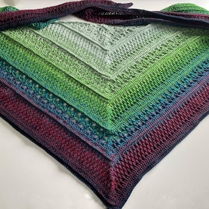 May include: A crocheted shawl with a gradient of colors, starting with a deep burgundy and transitioning to a light green. The shawl has a delicate lace pattern and a fringed edge.