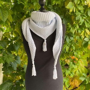 May include: A light blue crocheted scarf with tassels on a black mannequin. The scarf is draped around the mannequin's neck and has a decorative element in the center.