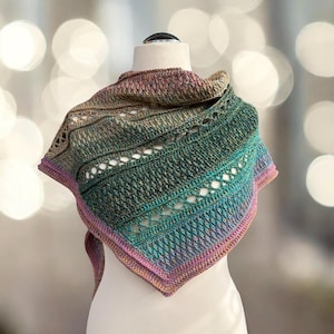 Könnte beinhalten: Ein handgefertigter, mehrfarbiger Schal, präsentiert auf einer Schaufensterpuppe. Der Schal zeigt einen Farbverlauf von Grün über Blau bis hin zu Rosa. Er hat ein strukturiertes Strickmuster mit Lochmusterdetails und einen rosa Rand.