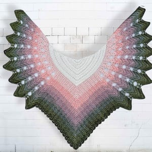 Op de afbeelding: Een handgemaakte sjaal met een zigzagpatroon. De sjaal heeft een kleurovergang van olijfgroen naar roze en grijs, met een wit midden. De randen hebben een geschulpte vormgeving.