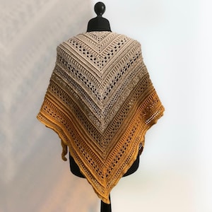 Può includere: Uno scialle all'uncinetto con un gradiente di colori beige, marrone e arancio. Lo scialle è di forma triangolare e presenta un delicato motivo a pizzo.
