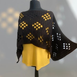 Puede incluir: Poncho de crochet negro con un patrón de panal. El poncho está en un maniquí y tiene una camiseta amarilla debajo.