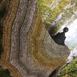 May include: A knitted shawl with a chevron pattern in shades of brown and gold. The shawl is draped over a black mannequin.