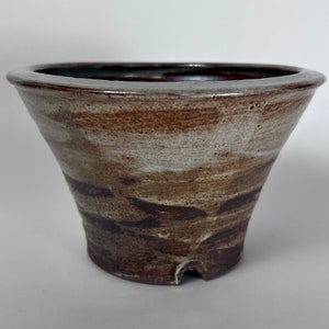 May include: A brown and white ceramic planter with a wide, rounded top and a narrow base. The planter has a mottled glaze with brown and white streaks.