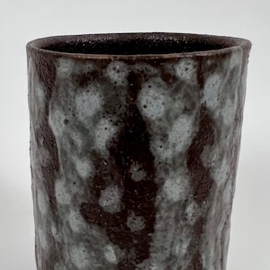 May include: A brown ceramic cup with a white and gray speckled glaze. The cup has a cylindrical shape and a slightly flared rim.