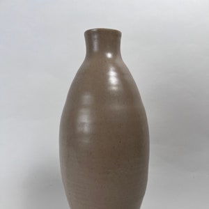 May include: A light brown ceramic vase with a rounded body and a narrow neck.