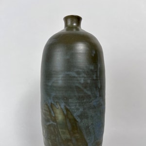 May include: A tall, dark gray ceramic vase with a mottled glaze. The vase has a rounded body and a narrow neck.