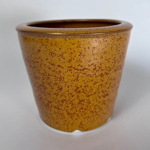 May include: A small, speckled, terracotta-colored ceramic planter with a rounded bottom and a slightly flared rim.