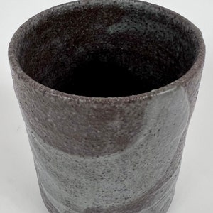 May include: A dark gray ceramic mug with a textured surface and a light gray glaze. The mug has a wide, round opening and a slightly flared lip.