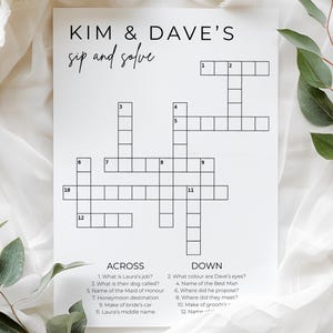 Puede incluir: Un papel blanco con un crucigrama para la boda de Kim y Dave, con el texto "sip and solve" encima del rompecabezas. El rompecabezas incluye pistas como "¿Cuál es el trabajo de Laura?" y "¿Dónde propuso matrimonio?" Hojas verdes y tela blanca en el fondo.