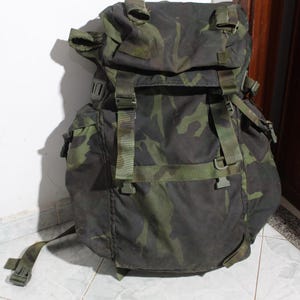 Könnte beinhalten: Ein großer grüner und brauner Tarnrucksack mit mehreren Riemen und Schnallen.