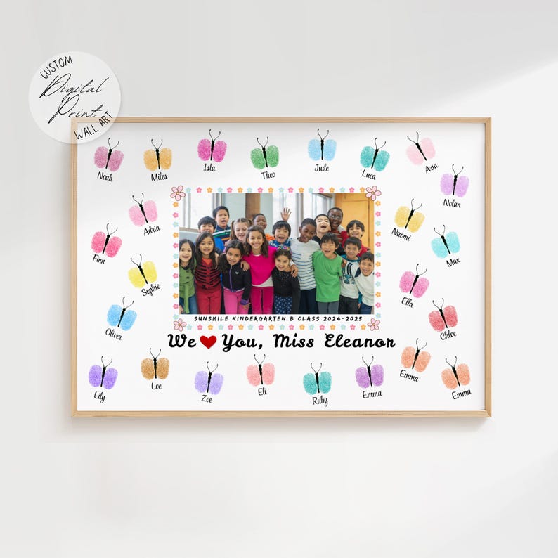 May include: A framed print featuring a class photo surrounded by colorful fingerprint butterflies. The text reads "We ❤️ You, Miss Eleanor" and "SUNSMILE KINDERGARTEN & CLASS 2024-2025". The print has a wooden frame and a white background.