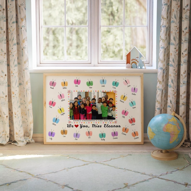 May include: A framed photo featuring a group of children, surrounded by colorful butterfly illustrations and names. The text "We ❤️ You, Miss Eleanor" is displayed below the photo, with the words "Sunshine Kindergarten & Class 2024-2025" above it.