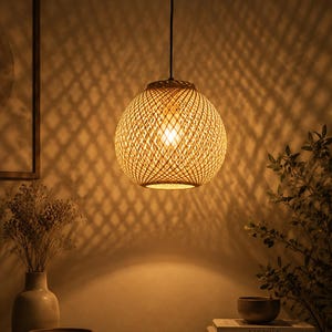 Könnte beinhalten: Eine kugelförmige Pendelleuchte aus geflochtenem Rattan. Das Licht hängt an einem schwarzen Kabel und strahlt warmes Licht aus. Der Schirm hat ein Rautenmuster. Das Licht hängt über einer Holzoberfläche.