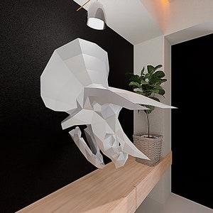 May include: A white origami triceratops sculpture hangs on a black wall above a wooden shelf with a potted plant.
