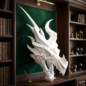 May include: A white, low-poly geometric dragon head sculpture mounted on a dark green panel. The dragon features sharp, angular facets, prominent horns, and an open mouth with visible teeth, creating a structured, multi-faceted appearance.