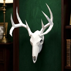May include: A white geometric deer skull wall mount featuring a faceted, low-poly design with large, branching antlers. The sculpture is constructed from flat, angular planes that form the shape of a deer head, creating a sharp, modern appearance.
