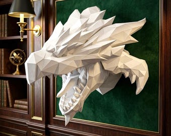 May include: A white, low-poly geometric dragon head sculpture mounted on a dark green velvet panel. The sculpture features sharp, angular facets, a wide-open mouth with visible teeth, and a pointed snout, creating a structured, three-dimensional form.